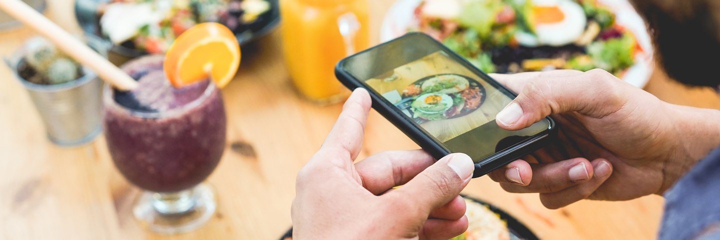 Hands photographing a brunch plate with a phone at a restaurant table