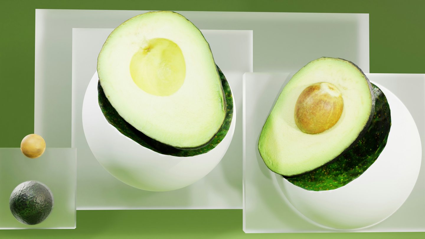 Two halved avocados resting on white spheres in front of frosted glass panels on a green background, with a whole avocado and an avocado stone in a smaller glass box