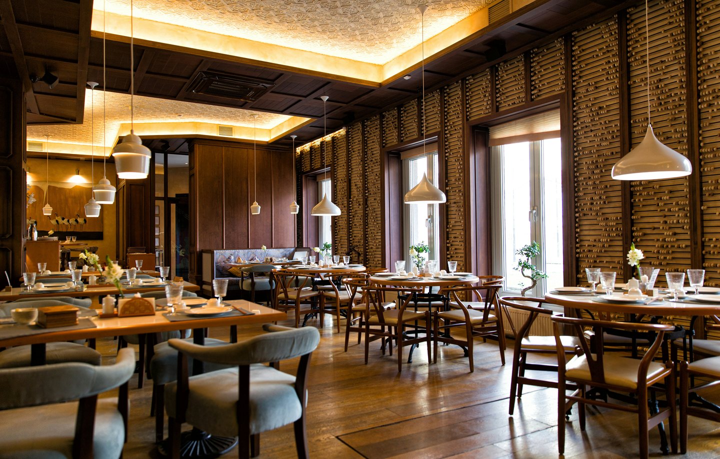 An empty restaurant dining room with set tables, pendant lights and wood panelling.
