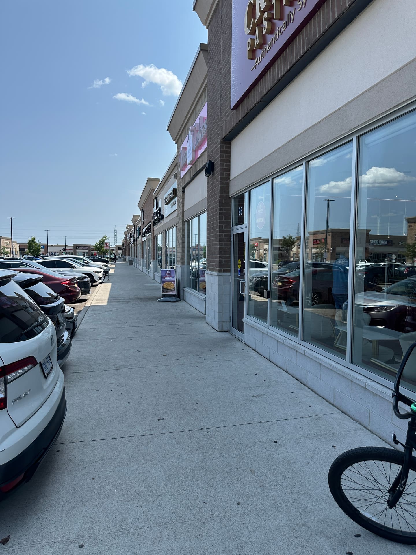 Sidewalk alongside Ridgeway bakery storefronts, with parked cars beside the walkway