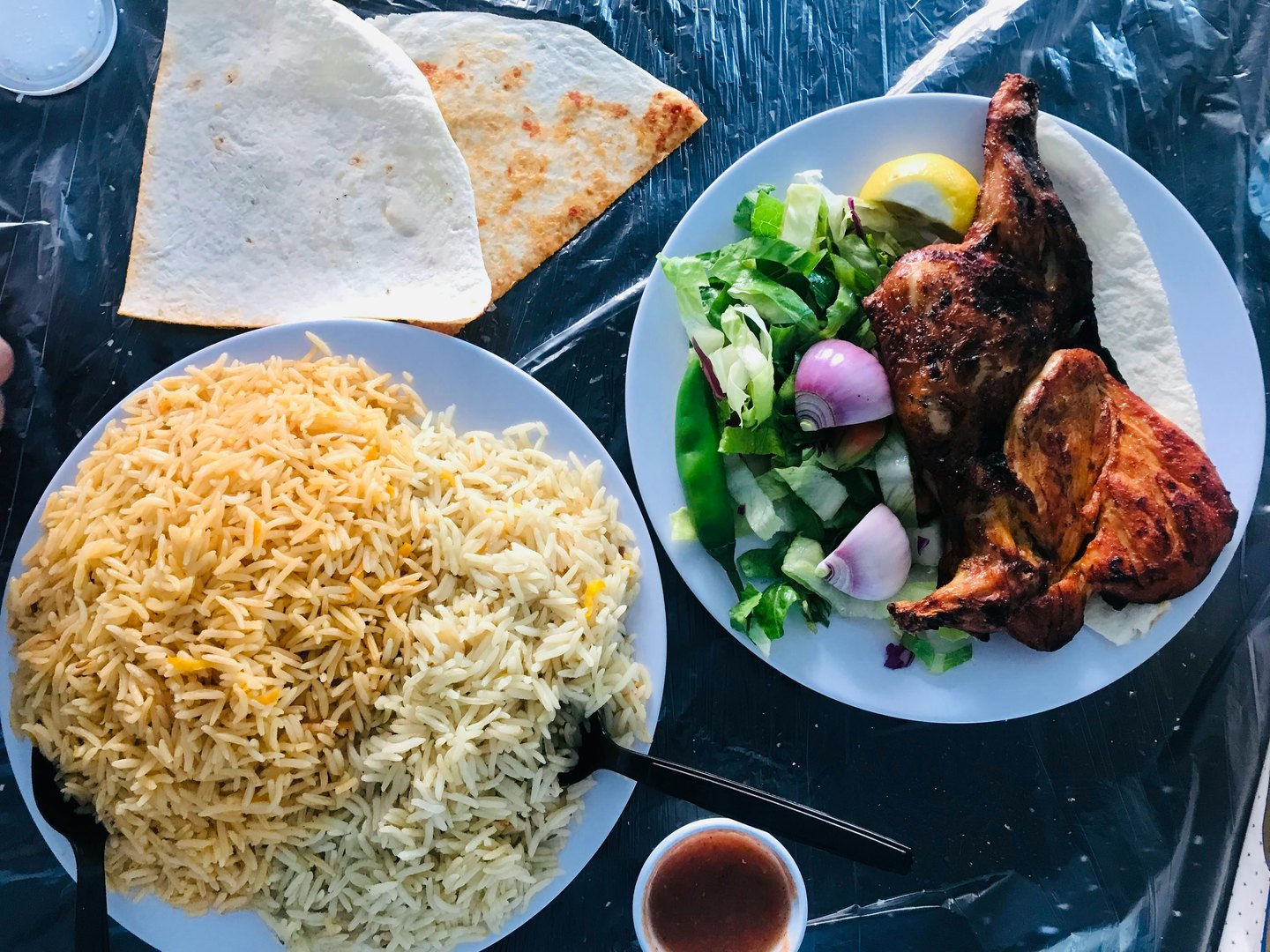 Grilled chicken with salad, a plate of rice, flatbread and a small bowl of sauce.